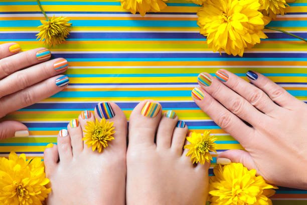 Colorful striped fashion summer pedicures and manicures for women's short nails with yellow flowers.Nail art.