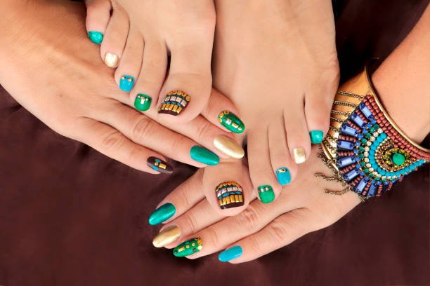 Multicolored pedicure and manicure with rhinestones on oval long female nails.Nail design with turquoise, brown, blue and gold nail Polish.