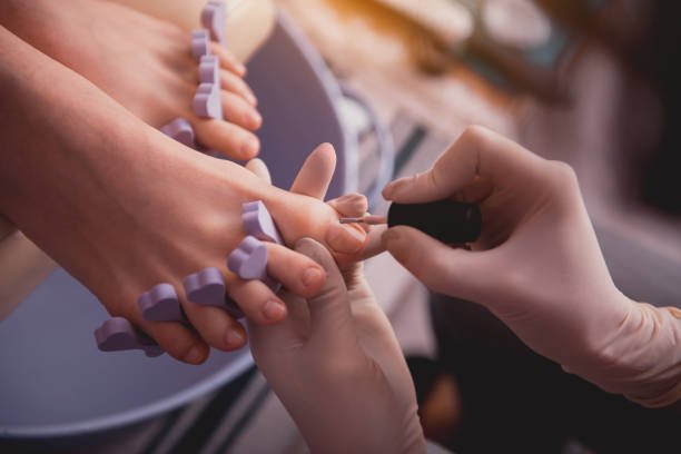 Top view close up female manicurist hand in gloves painting nails on feet of lady. Treatment concept